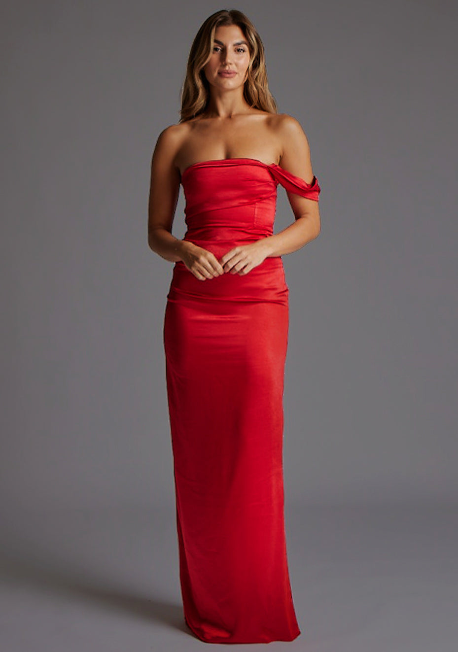Front image of a blonde model wearing a Red Maxi Dress with a  one-sleeve off-shoulder design, crafted with luxurious satin fabric, a design features Vesper Roselie Red Maxi Dress
