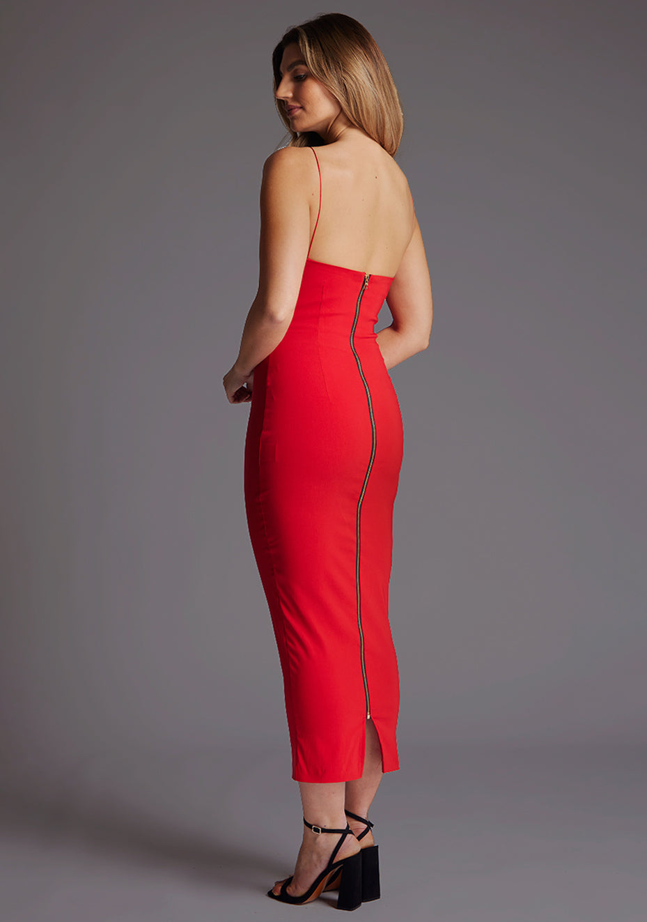 Back quarter image of a model wearing a red midaxi dress with a scoop neckline, thin straps, a bodycon fit and centre back invisible zip and small keyhole cut-out at bust. The design featured is the Vesper Roxanne Red Midaxi Dress.