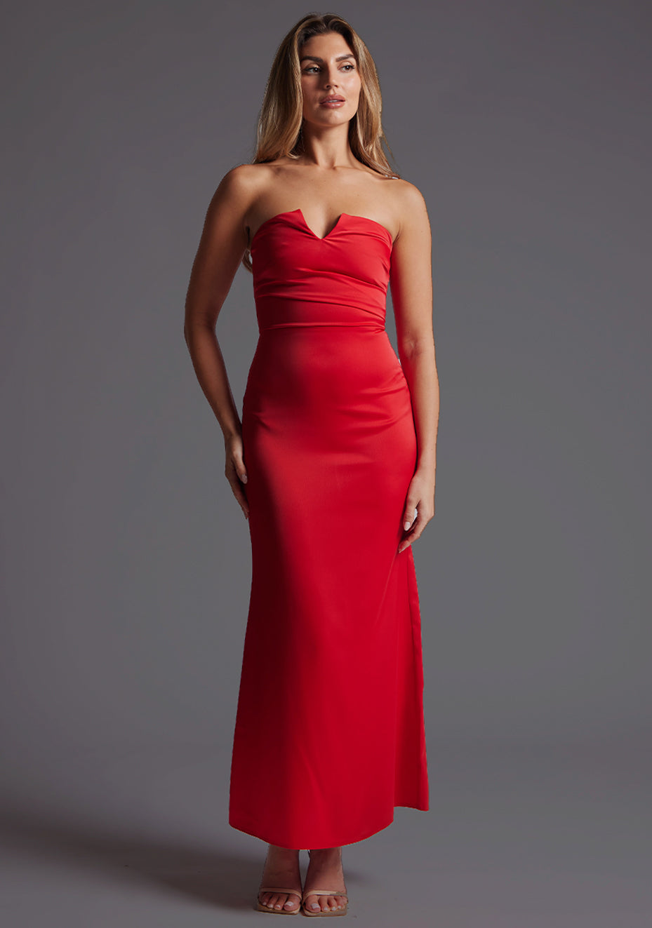 Front image of a blonde model wearing a red midaxi dress with a strapless design, front cutout with a sleek and slim fit silhouette. The design featured is the Vesper Sabine Red Midaxi Dress