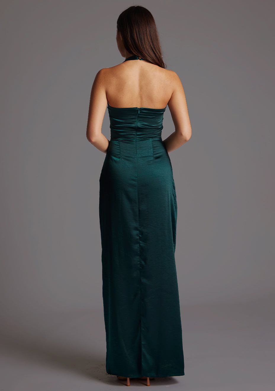 Back image of a  model wearing a pine maxi dress with a halter cowl neck exudes sophistication, while the lustrous satin fabric offers a luxurious touch. The design featured is the Vesper Saige Pine Satin Green Maxi Dress.