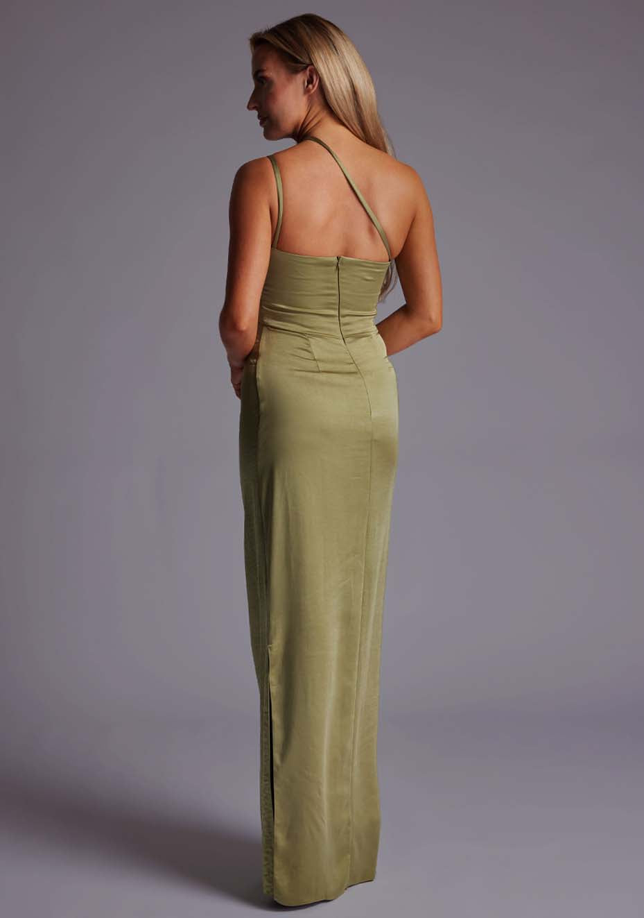 Back quarter image of a model wearing an olive satin maxi dress with a cross strap detail, pleats detailing at the front bust and delicate side skirt split. The design featured is the  Vesper Solange Olive Satin Maxi Dress.