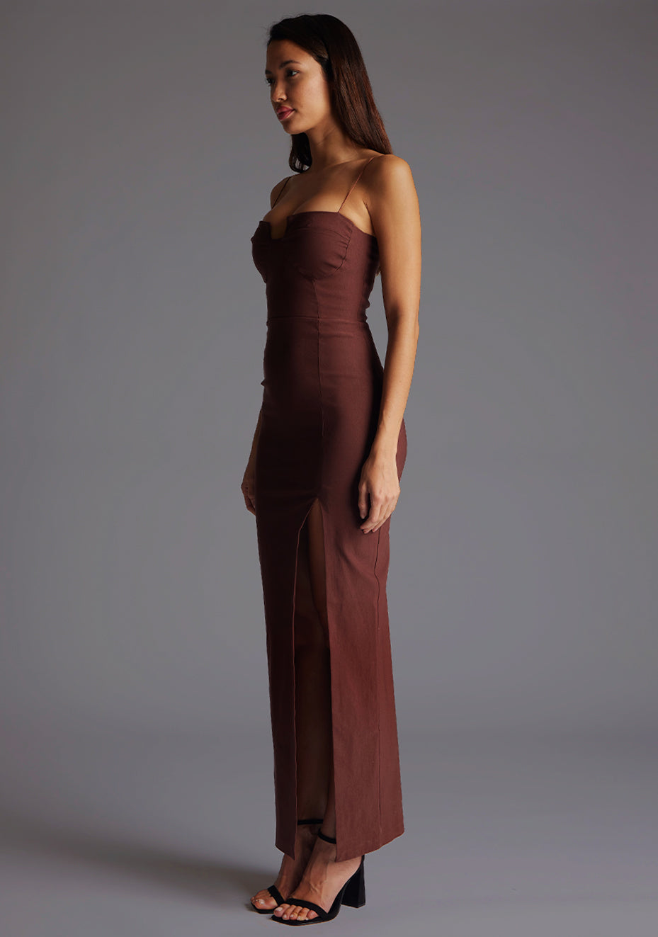 Front quarter image of a model wearing a chocolate maxi dress with a chic square neckline with an elegant cutout, complemented by delicate thin straps, back zip ensures a seamless fit and a front skirt split. The design featurd is the Vesper Suki Chocolate Maxi Dress.