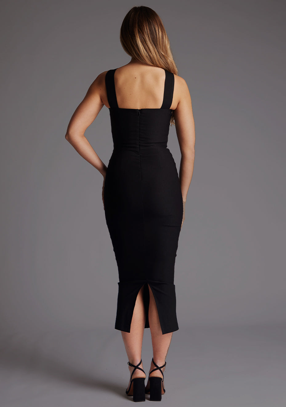 Back image of a  model wearing a black midaxi dress with a bodycon fit, sweetheart neckline with wide straps from centre of bust to over shoulder. The design featured is the Vesper Suzanne Black Midaxi Dress.