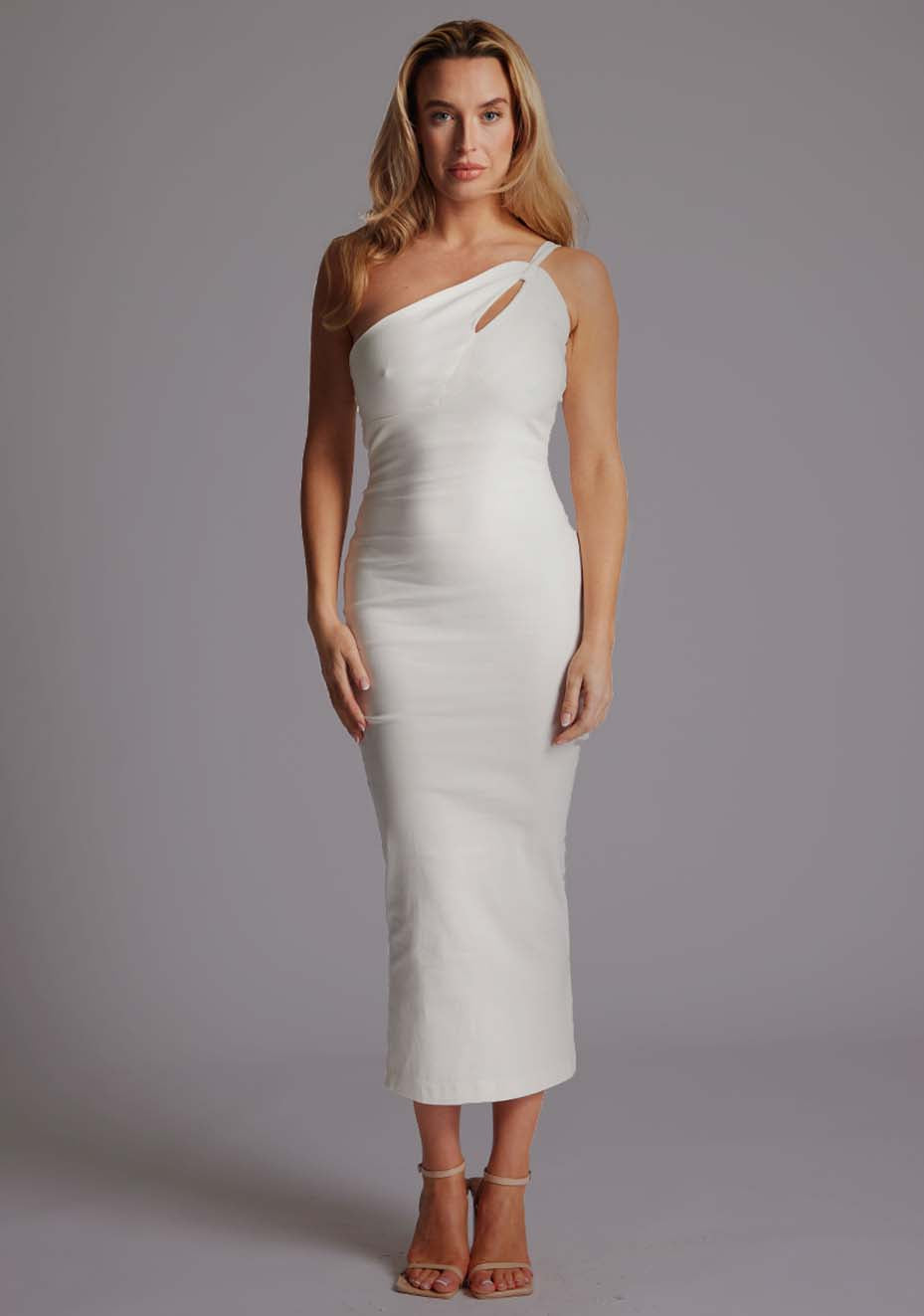 Front image of blonde model wearing a ivory midaxi dress with an unique one-shoulder design, asymmetric neckline with a small cut-out and a bodycon fit, finished with a statement centre back gold zip. The design featured is the Vesper Tasha Ivory One Shoulder Midaxi Dress.