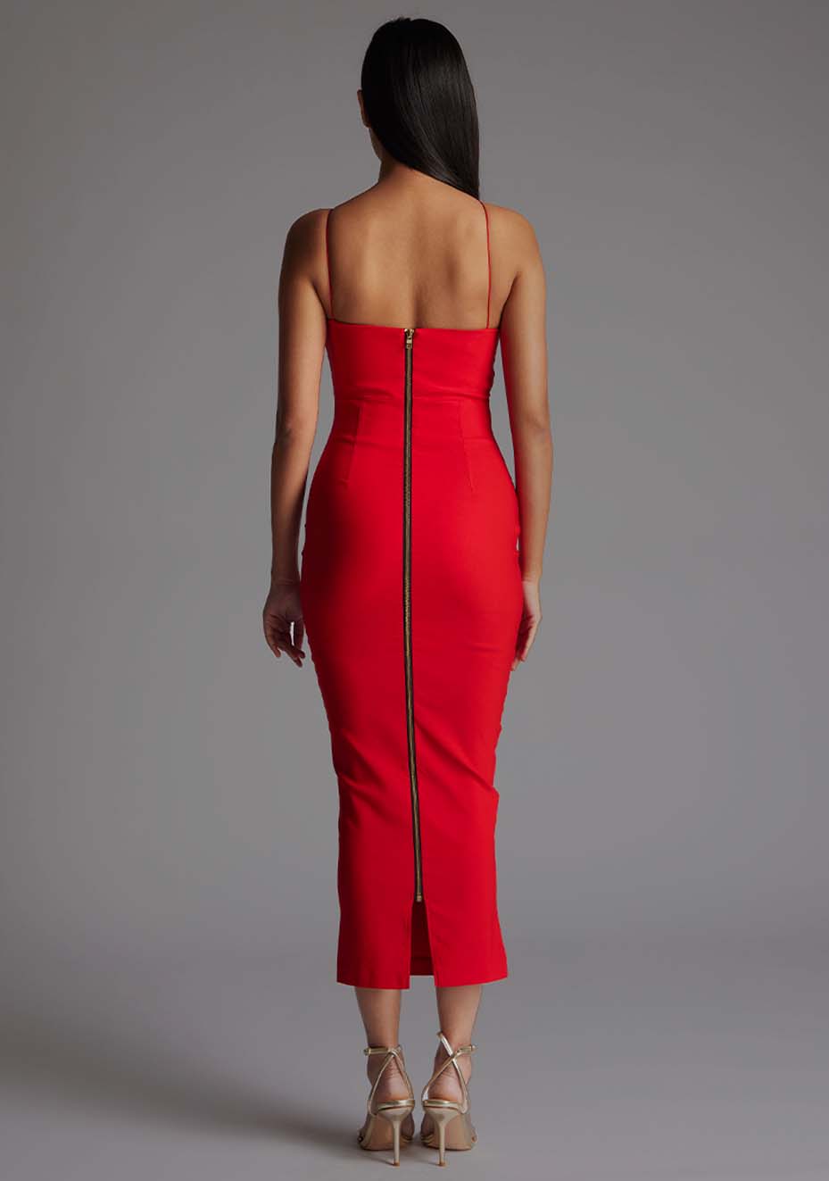 Back image of a model wearing a red midaxi dress with a asymmetric neckline and one shoulder with double thin strap detail on shoulder and across chest create a unique and elegant design, while the side waist cut-out and centre back gold zip add an extra touch of glamour. The design featured is Vesper Whitney Red Midaxi Dress