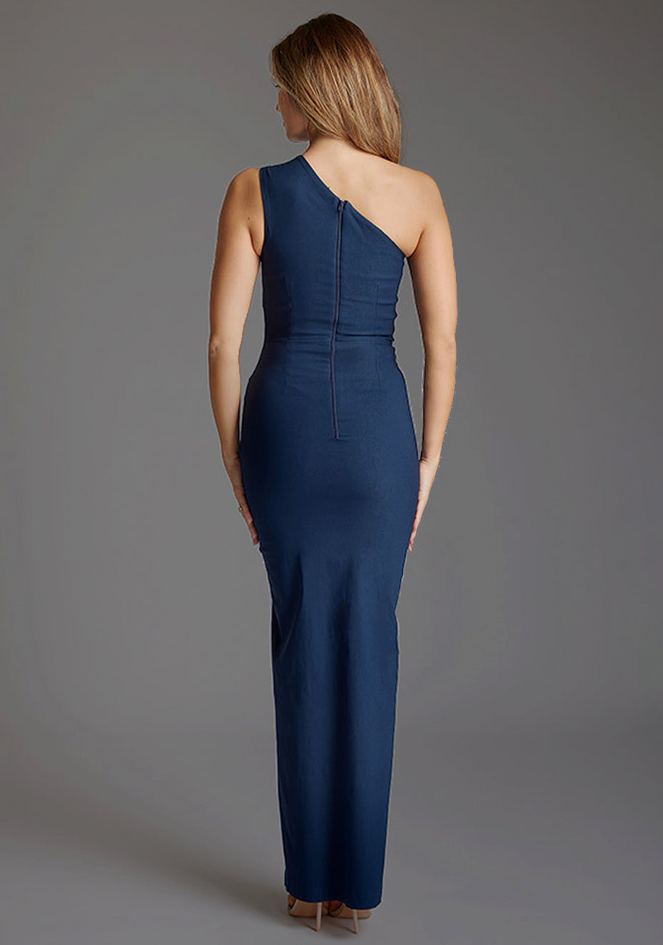 Back image of blonde model wearing a Navy Maxi Dress with an asymmetric neckline with thigh-high leg split and cut out one shoulder design. The design featured is the Vesper Wren One Shoulder Navy Maxi Dress