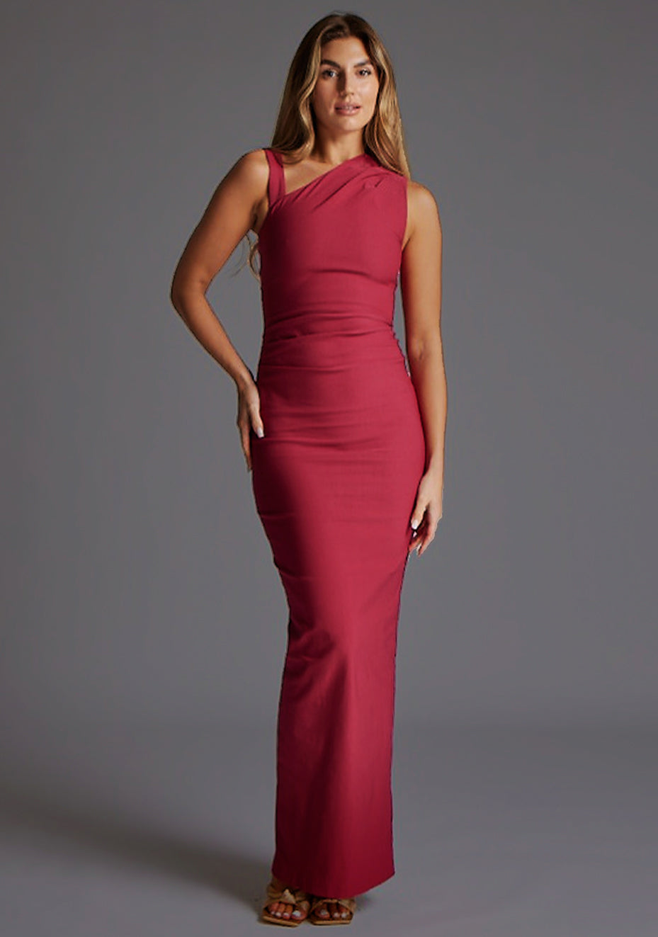 Front image of a model wearing a raspberry asymmetric maxi dress with a asymmetric neckline silhouette, back skirt split and ruched detailing enhances the dress's allure. The design featured is the Vesper Wyatt Raspberry Asymmetric Maxi Dress.