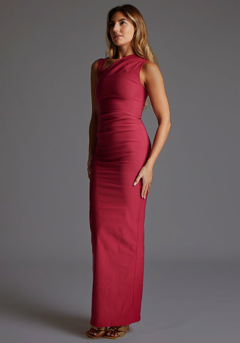 Front quarter image of a model wearing a raspberry asymmetric maxi dress with a asymmetric neckline silhouette, back skirt split and ruched detailing enhances the dress's allure. The design featured is the Vesper Wyatt Raspberry Asymmetric Maxi Dress.