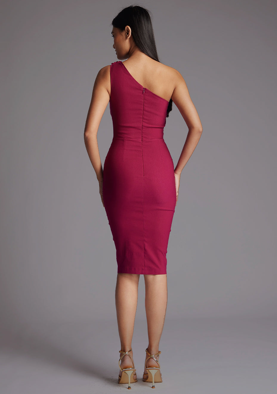 Back image of blonde model wearing a berry midi dress with an alluring one-sleeve design and a captivating asymmetric cut, and a discreet back zip. The design featured is the Vesper Xyla Berry One Shoulder Midi Dress